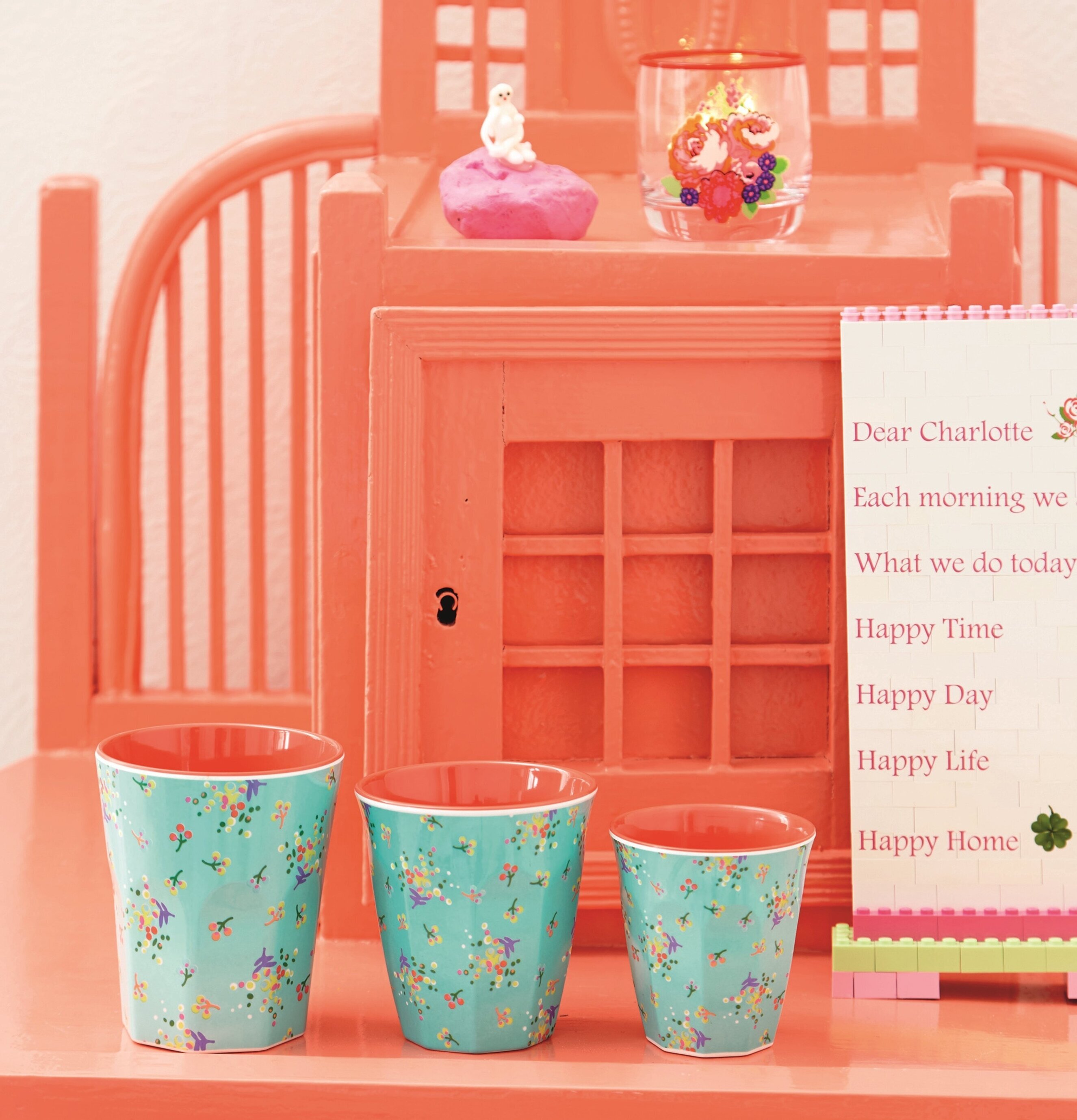 Mugg Aqua Blommor från Rice framför en korallfärgad möbel