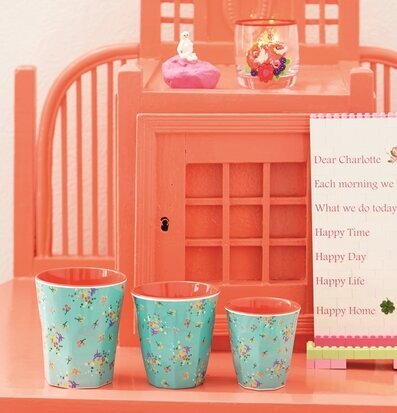 Mugg Aqua Blommor från Rice framför en korallfärgad möbel